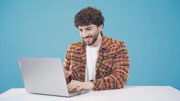 bonito jovem homem com encaracolado cabelo usando computador portátil. atraente jovem homem alegria, trabalhando a partir de lar, compras on-line, assistindo videos ou escrevendo e-mails.