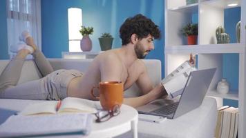 Attractive naked young man working in home office using laptop, taking notes. Handsome and attractive young man using laptop alone at night at home working in home office concept. video
