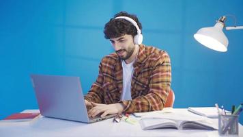 Happy and pleasant relaxed male student doing research online using laptop, taking notes, writing essay, preparing for test exam. video