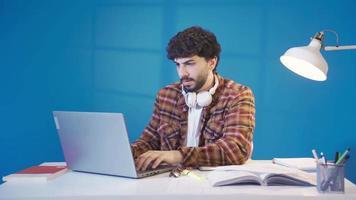 réfléchi et confus Masculin étudiant en train d'étudier en utilisant portable. Beau souriant Jeune étudiant séance à bureau travail avec documents, idée de génie Créatif projet avec recherche. video