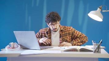 intelligent et travailleur Masculin étudiant obtient le sien devoirs ou cours terminé vite et vivement. Jeune Beau Université étudiant en portant portable à table à la recherche à livres et Remarques rapidement. video