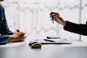 A car rental company employee is handing out the car keys to the renter after discussing the rental details and conditions together with the renter signing a car rental agreement. Concept car rental. photo