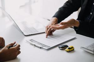 A car rental company employee is handing out the car keys to the renter after discussing the rental details and conditions together with the renter signing a car rental agreement. Concept car rental. photo