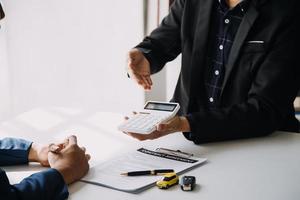 A car rental company employee is handing out the car keys to the renter after discussing the rental details and conditions together with the renter signing a car rental agreement. Concept car rental. photo