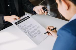 A car rental company employee is handing out the car keys to the renter after discussing the rental details and conditions together with the renter signing a car rental agreement. Concept car rental. photo