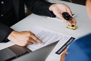 A car rental company employee is handing out the car keys to the renter after discussing the rental details and conditions together with the renter signing a car rental agreement. Concept car rental. photo