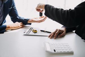 A car rental company employee is handing out the car keys to the renter after discussing the rental details and conditions together with the renter signing a car rental agreement. Concept car rental. photo