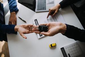 A car rental company employee is handing out the car keys to the renter after discussing the rental details and conditions together with the renter signing a car rental agreement. Concept car rental. photo