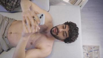 Naked and attractive young man using his smartphone. Model male. Handsome young man with a fit and fit body lying happily on the sofa, looking at his phone. video