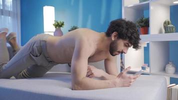 Naked handsome young man lying on armchair using smartphone, texting, surfing social media apps. Handsome young man with a fit and fit body lying happily on the sofa, looking at his phone. video