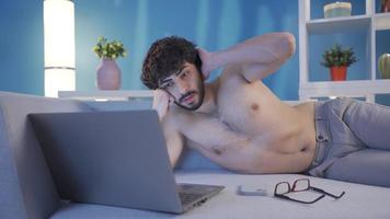 nudo giovane uomo nel bicchieri utilizzando il computer portatile solo a casa, digitando su tastiera del computer. giovane nudo bello uomo seduta su il pavimento a casa utilizzando il computer portatile. video