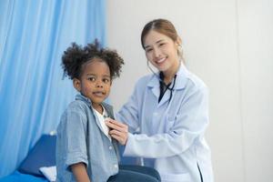 el niña se sienta en el del paciente cama para el doctor. foto