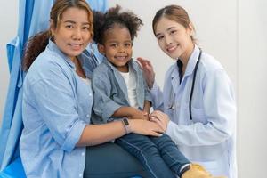 el niña se sienta en el del paciente cama para el doctor. foto