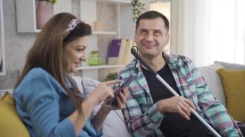 Blind man's vrouw is vertellen iets door op zoek Bij de telefoon. zijn vrouw vertelt iets naar de Blind Mens zittend Aan de sofa Bij huis door op zoek Bij de telefoon. ze babbelen en zijn gelukkig. video