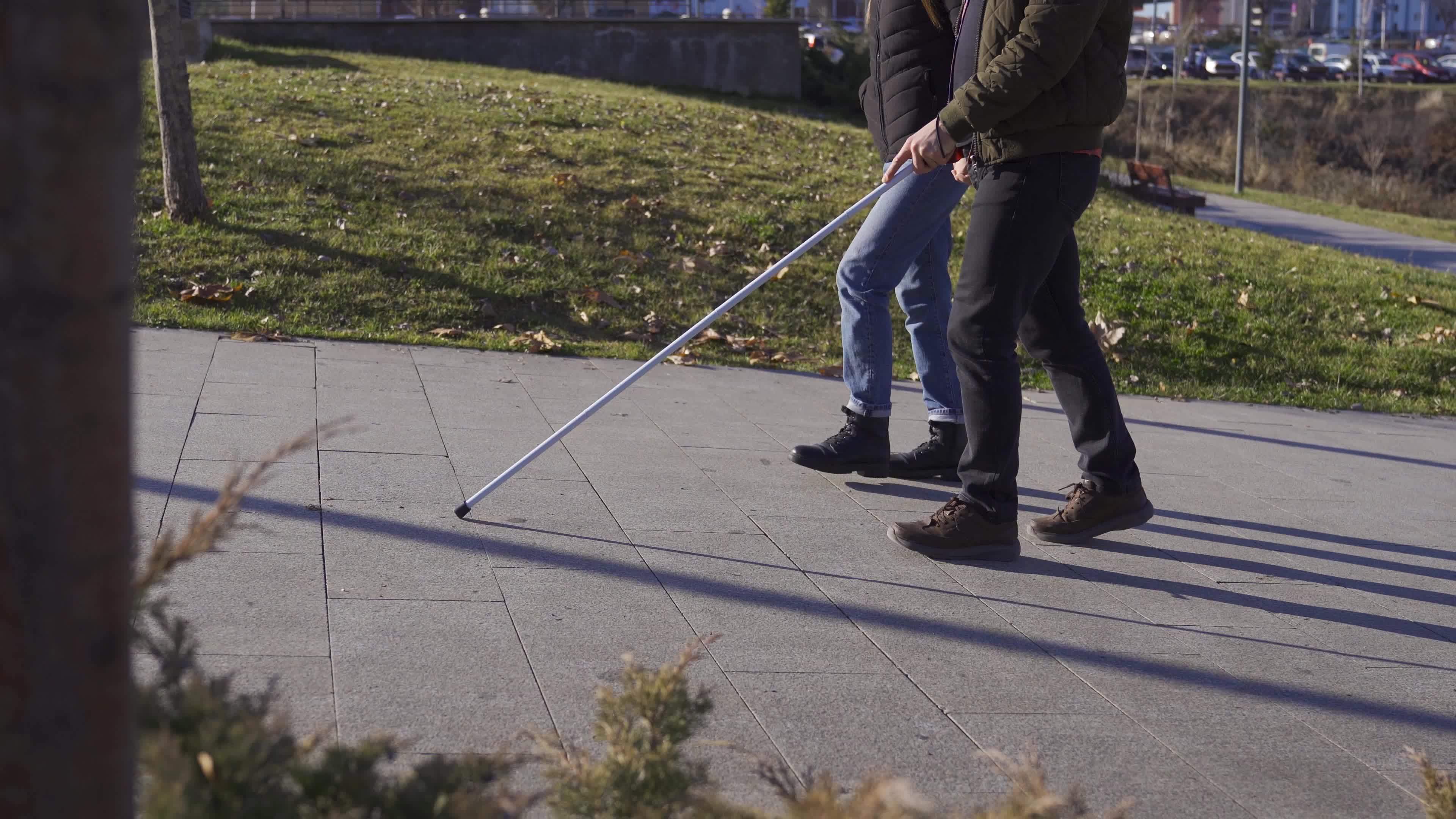 Blind man walking in the park with his wife. Blind man with a cane