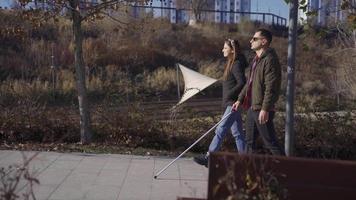 blind Mann Gehen im das Park mit seine Ehefrau im Herbst. ein blind Mann mit ein Gehen Stock ist Gehen im das Park mit seine Gattin. Sie sind glücklich. video