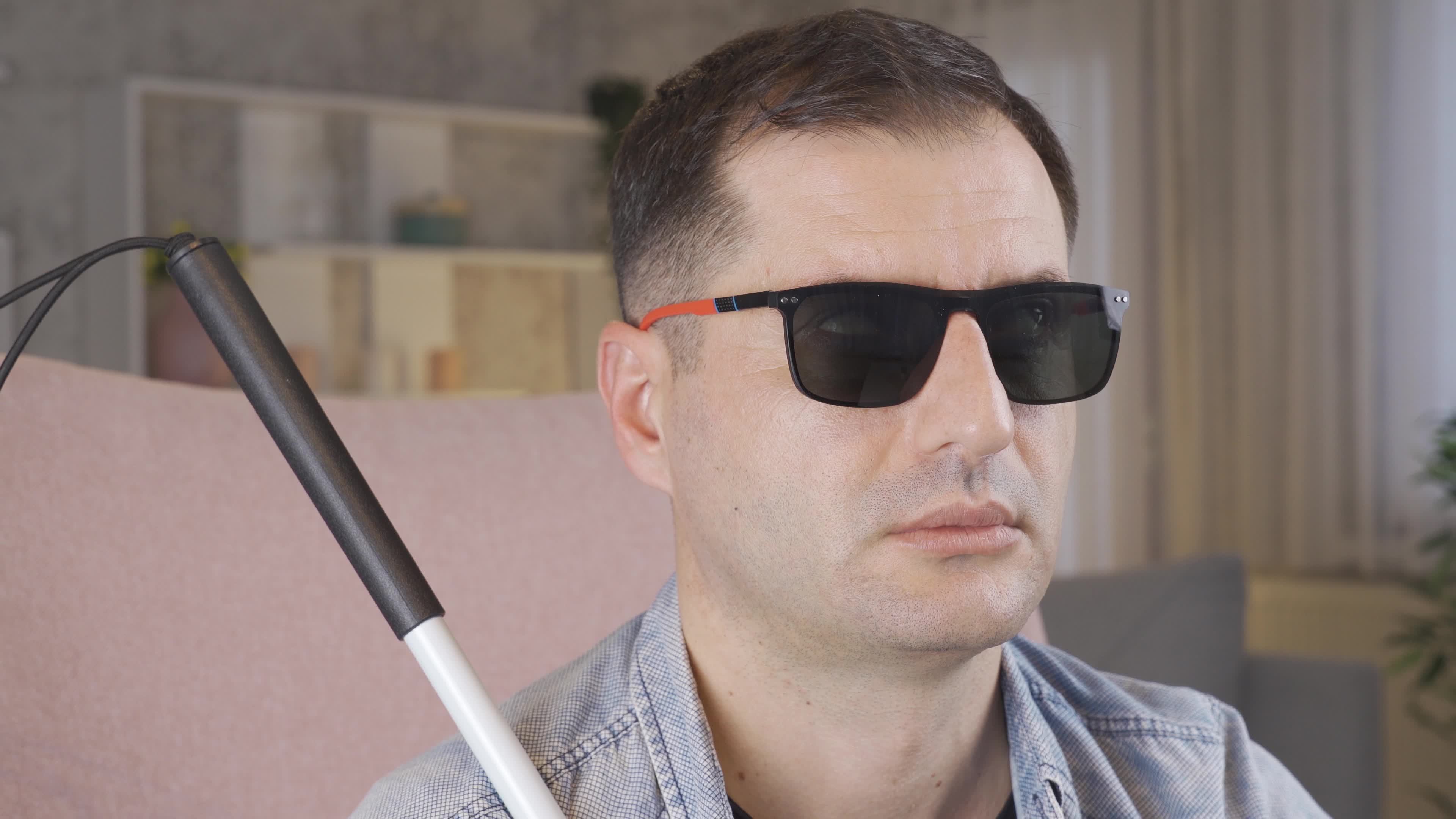 Blind man taking off his black glasses. Blind man sitting on sofa at