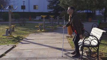 le aveugle homme séance sur une banc obtient en haut et départs marche. avec le Aidez-moi de le sien en marchant bâton, le aveugle homme obtient en haut de le sien siège et départs marche. ensoleillé journée dans l'automne. video