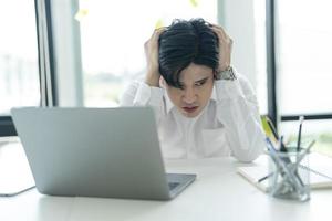 Young businessman sitting at his desk looking at the internet on his laptop Feeling stressed. photo