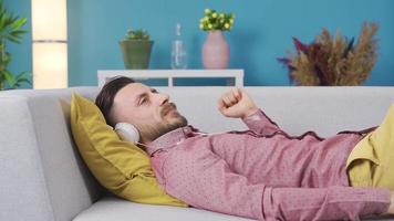 homme relaxant sur canapé à Accueil avec écouteurs écoute à musique, rêverie et heureux. homme mensonge sur canapé à Accueil repos et content écoute à la musique avec écouteurs. video