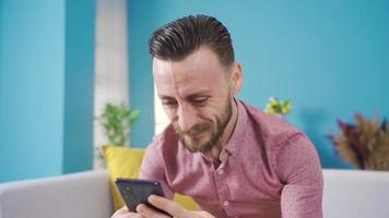 Happy young man using his smart mobile phone at home. Happy young man using smartphone, Texting, looking at social media posts. video