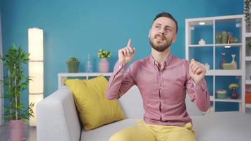 contento e allegro uomo danza e sognare a casa. allegro giovane uomo seduta su divano a casa e danza con gioia, gioia a contento notizia. video