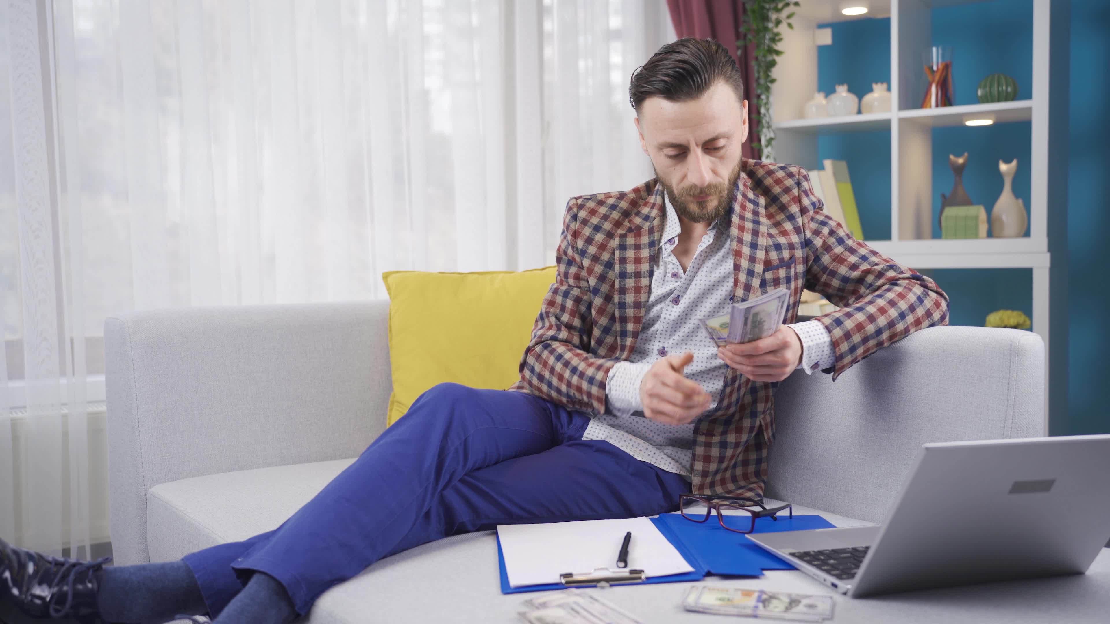 Businessman sitting on sofa at home counting his money and doing