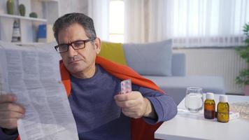 Sick and exhausted man reading the prospectus of the medicinal drugs he will use. Sick mature man is sluggish and exhausted at home, taking his medications, trying to maintain his health. video