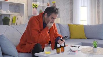 maduro hombre con gripe y frío enfermedad agotado a hogar, mirando a teléfono y Bebiendo curación y sano bebidas video