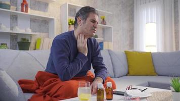 Mature sick man with throat irritation and pain massaging his throat with his hands. Man with sore throat is resting at home, drinking healthy and hot drinks. video