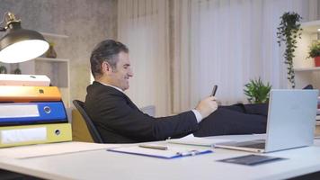 Mature businessman working in home office looking at phone with happy and smiling. Happy and elegant mature businessman using smart cell phone in home office, texting, using social media apps. video