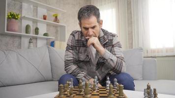 Thoughtful retired mature man playing chess at home alone executing strategy. The mature man, bored alone, plays chess, thinks, plays strategically. video