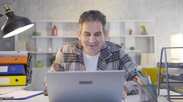 Mature man working in home office gets excited and happy while using laptop. Excitedly waiting mature man looking at laptop and happily continuing to work. video