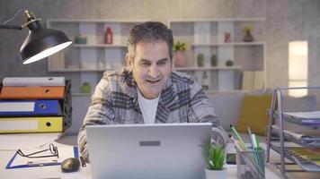 The mature man working in the home office is excited and delighted by the event he is waiting for. Mature man excitedly waiting by laptop rejoices and smiles. video