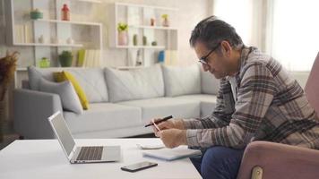 Man looking at bills doing calculations with calculator at home. Mature man plans the budget. Mature man sitting on sofa at home calculation online loan debt payments and shopping receipts. video