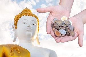 Money in hand and big Buddha statue ,Coins Savings Donation Investment photo