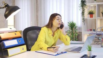 Busy young woman working at home at laptop talking on phone. Talking to Friend, Talking to Parents. video