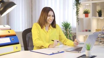 giovane donna Lavorando con un' il computer portatile nel sua casa ufficio è sorpreso e Contentissimo di che cosa lei vede, guardare a il telecamera. video