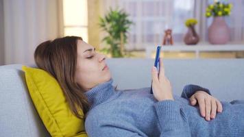 Young woman looking at her smartphone on the sofa is unhappy and depressed. Depressed young woman resting on sofa at home and wants to spend time looking at phone. video