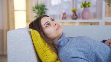 nachdenklich jung Frau ruhen auf Sofa beim Zuhause suchen beim Kamera. jung Frau ruhen auf das Sofa denkt und wendet sich ihr Kopf zu aussehen beim das Kamera. video