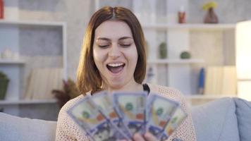 Happy young woman with money looking at her smartphone, making money, spending money. Young woman holding money happily looking at her smartphone and thinking thoughtfully. video