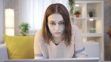 konzentriert und ernst jung Frau beim Zuhause suchen beim Laptop. jung Frau Sitzung auf Sofa beim Zuhause mit Laptop konzentriert und ernst. freiberuflich jung Frau, weiblich Schüler tun Forschung. video