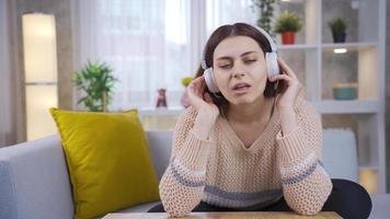 Positive high school or college student listening to music with headphones and relaxing. Young woman listening to music with headphones closed eyes on comfortable sofa. video