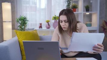 riflessivo preoccupato giovane donna Lavorando su computer portatile, guardare a documento e scartoffie. giovane donna Lavorando a partire dal casa è sorpreso e stordito di che cosa lei vede su lavoro d'ufficio e il computer portatile. video