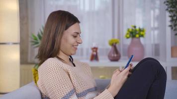 hermosa joven mujer utilizando teléfono inteligente a hogar sonriente felizmente. joven mujer participación teléfono inteligente teniendo divertido utilizando móvil aplicaciones riendo a móvil teléfono pantalla. video