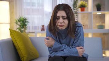 Sad young woman sitting on sofa feeling unhappy, having unpleasant thoughts, suffering because of life problems. video