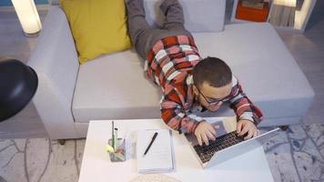 enano hombre trabajando en computadora acostado abajo a hogar. enano humano trabajando en computadora. él toma notas en un cuaderno. video