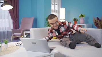 Desativado anão jovem homem feliz e alegre usando computador portátil, deitado em sofá e em repouso. anão, aluna ou trabalhador autonomo jovem homem trabalhando a partir de casa em computador portátil. video