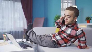 Cheerful and funny disabled dwarf young man chatting on the phone at home. Disabled dwarf young man talking on phone lying on sofa at home and resting. video