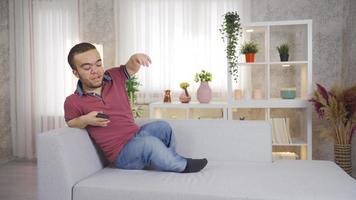 jung Zwerg Mann Sitzung auf Sofa beim Zuhause und mit Smartphone. jung Mann mit Zwergwuchs sitzt auf das Sofa beim Zuhause und beginnt mit seine Smartphone. video